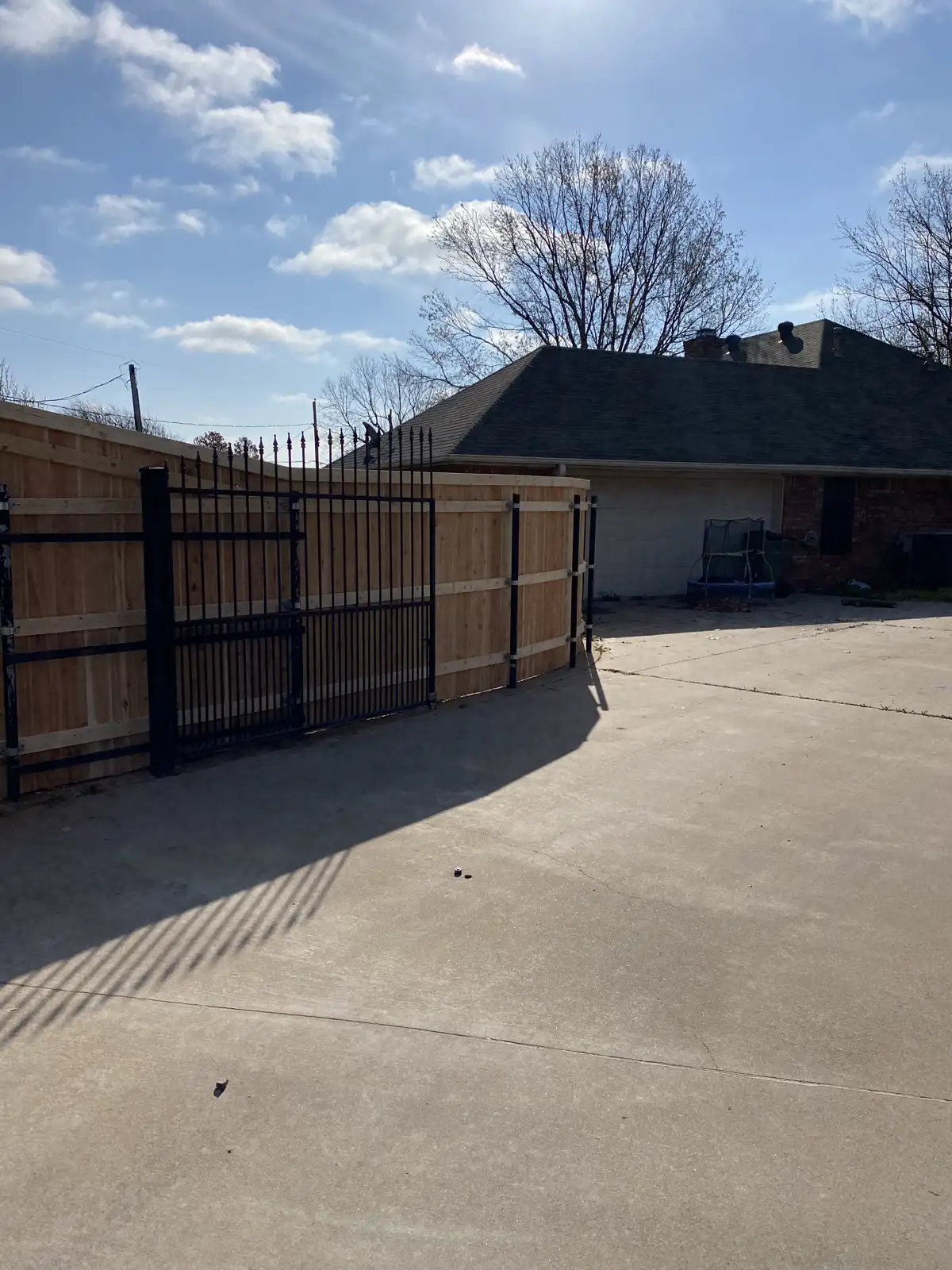 Black metal driveway gate installed with a privacy fence in Wichita Falls, TX